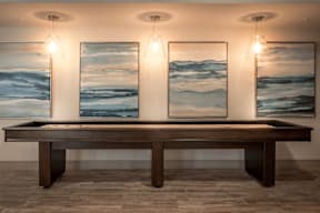 A long brown table is in front of three framed landscape paintings.