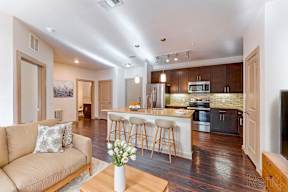 A well-lit kitchen with a breakfast bar and a living room with a couch.