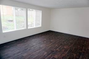 an empty room with wood flooring and two windows