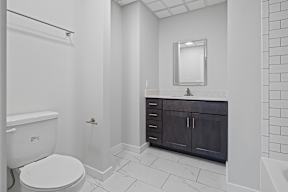 A white toilet is in a bathroom with a white tile floor and a white shower curtain.