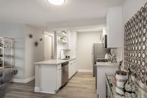 Apartments in Hollywood, CA, with In-Unit Washer and Dryer - Candela - Kitchen with Luxury Vinyl Plank Flooring, Customized White Cabinetry, Stainless Steel Appliances, Quartz Countertops, Shelves, Home Decor, and Kitchen Island with Single Sink and Gooseneck Faucet.