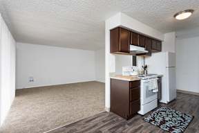 an empty living room and kitchen with white appliances and wood flooring