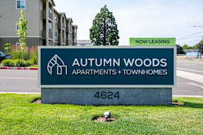 A sign for Autumn Woods Apartments and Townhomes is displayed in front of a building.