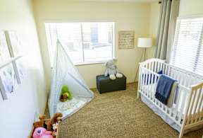 A baby's room with a white crib, a green ottoman, a teal tent, and a teddy bear.