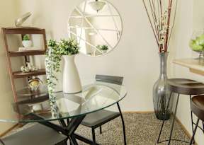 A glass table with a white vase and a black chair in the middle of it.