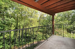 A balcony with a metal railing and a view of a wooded area.