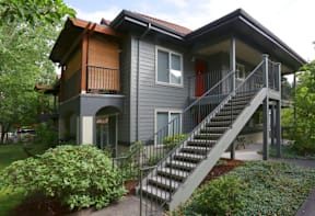 A grey house with a red door and a staircase leading to the second floor.