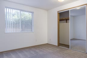 an empty bedroom with a large window and a mirrored closet