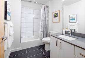 Luxury 1 BR Apartments in Portland OR - Couch9 Apartments - Bathroom with Large Mirror, White Cabinetry, and Large Grey Tile Flooring