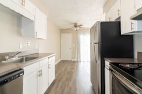 A black refrigerator stands in a kitchen with white cabinets and a sink.
