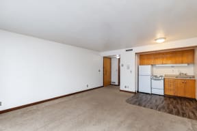 the living room and kitchen of an apartment with white walls and wood floors