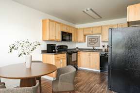 A kitchen with a black refrigerator, wooden cabinets, and a table with chairs.