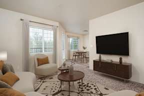 A living room with a white couch, a brown coffee table, and a large flat screen TV mounted on the wall.