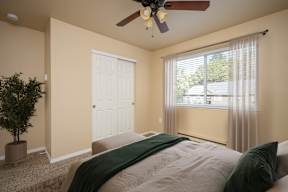 A bedroom with a bed, a ceiling fan, and a window with curtains.