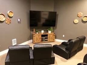 A living room with a large TV, a wooden entertainment center, and black leather chairs.