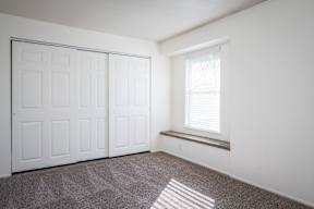 A room with a white door, a window with blinds, and a bench against the wall.