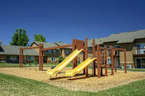 A playground with a yellow slide in front of a building.