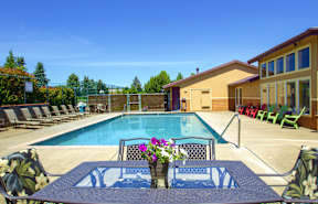 A pool surrounded by chairs and a table with flowers on it.