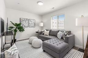 A living room with a grey couch, a white ottoman, and a television.