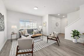 A living room with a grey couch, two wooden chairs, and a striped rug on faux wood flooring.