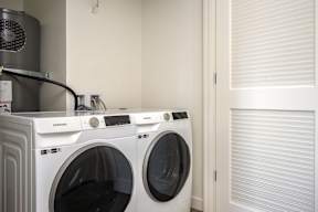 Two white Samsung front load washing machines in a laundry room.