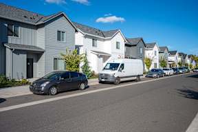 A street with a white van and a grey car parked on the side.