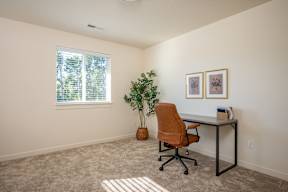 A room with a desk, chair, and a plant.