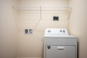 A white dryer is sitting in a small room with a clothes drying rack above it.