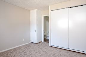A white closet with a door open to a bathroom.