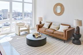 A living room with a brown couch, a white chair, and a round table with a yellow object on it at The Anthem at Square 10 Apartments, New Haven, 06510