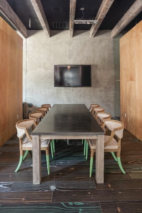 a large wooden table and chairs with green legs in a room with concrete walls and a tv  at Iron Works Sono, Norwalk, CT