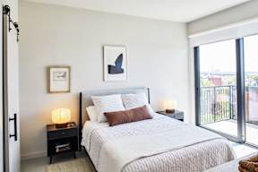 A bedroom with a large bed, a nightstand with a lamp, and a picture on the wall.