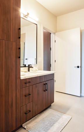 A bathroom with a white door and a brown cabinet with a mirror above it.