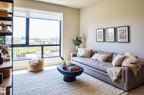 A living room with a grey couch, a round table, and a large window.