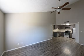an empty living room with a ceiling fan and a kitchen in the background