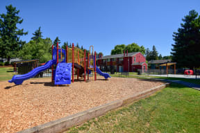 a playground with a blue slide and a red building in the background