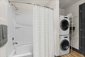 A white bathroom with a shower curtain and a washing machine.