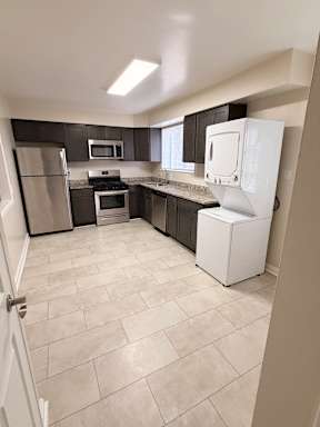 A kitchen with a white refrigerator, black cabinets, and a tiled floor.