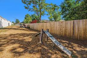 A wooden seesaw in a backyard with a dirt ground.