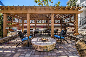 A wooden pergola with a fire pit in the middle of a patio.