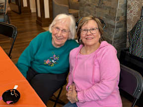 Two women wearing glasses and sweaters are sitting at a table.