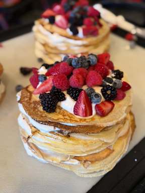 A stack of pancakes topped with berries and whipped cream.