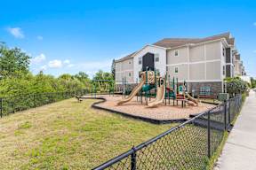 A playground with a slide and a green fence in front of a building. at Mode at Melbourne Apartments, Melbourne, Florida