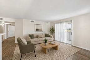 A living room with a grey armchair, a brown coffee table, and a beige sofa with a painting on the wall.