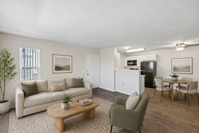 A living room with a white couch, a green armchair, a wooden coffee table, and a dining table with chairs.