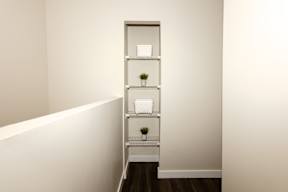 A white shelf with three shelves holding a plant and a white bowl.