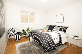 A bedroom with a bed, chair, and plant.