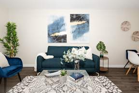 A living room with a blue couch, a coffee table with a vase of flowers, and a painting on the wall.