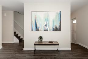 A painting hangs on the wall above a table with a cactus and a book on it.