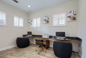 a desk with two computers and two chairs in a room with white walls and white shutters